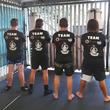 Four people wearing matching team shirts standing with their backs to the camera in a boxing gym.