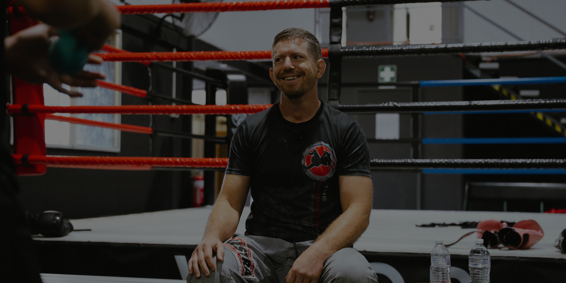 Man sitting in a boxing ring with gym equipment in the background