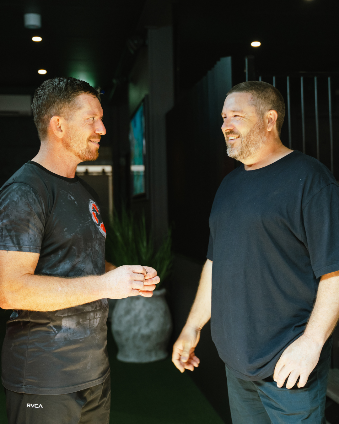 Two men engaged in a grounded, supportive conversation inside a modern space.